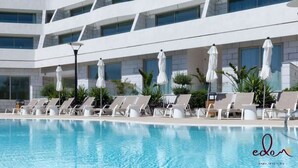 Zona de piscina d'un hotel modern amb nombroses gandules i ombrel·les, envoltada per un edifici de diversos pisos amb grans finestres.