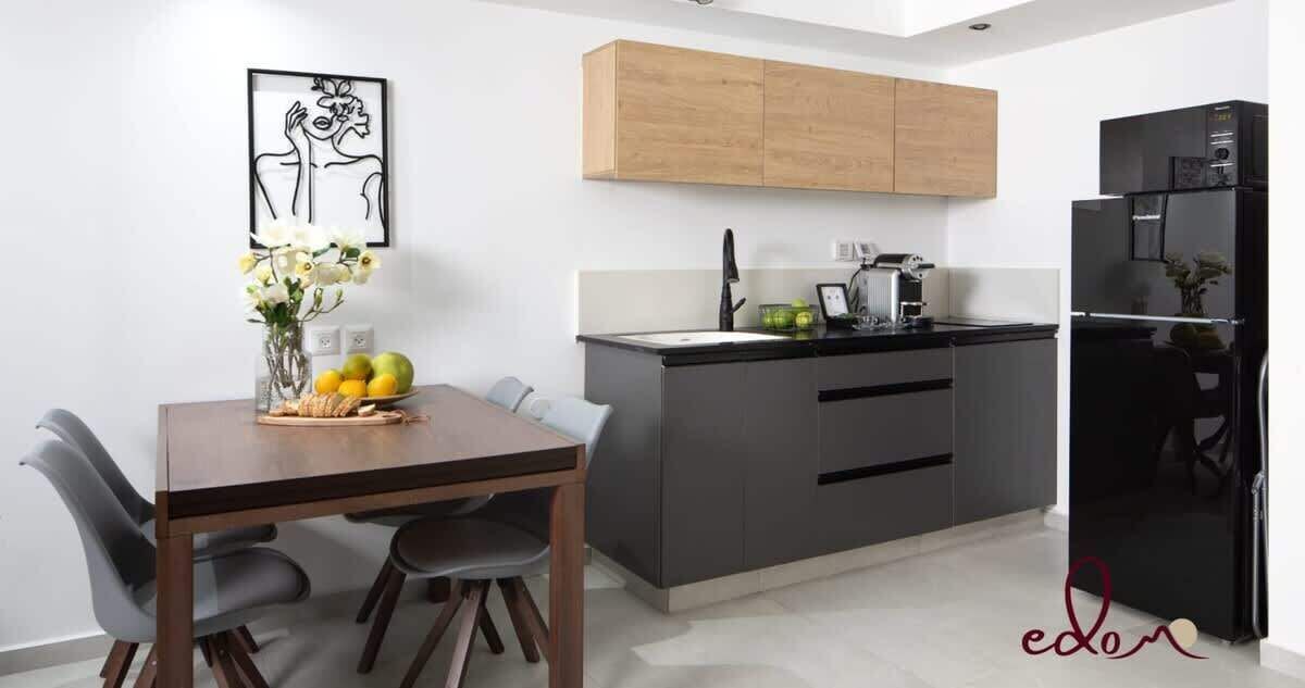 Una cocina moderna con armarios grises, un refrigerador negro y una zona de comedor con mesa y sillas de madera.