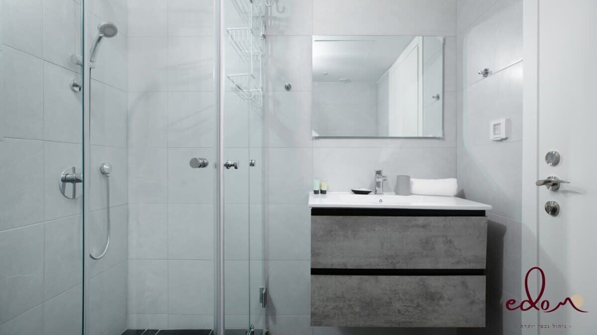 A modern bathroom with a glass shower enclosure, a white sink with a grey countertop, and a large mirror above the sink.