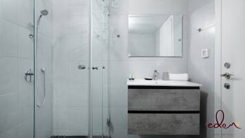 A modern bathroom with a glass shower enclosure, a white sink with a grey countertop, and a large mirror above the sink.
