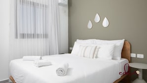 Cama bem arrumada com lençóis e almofadas brancas, mesa de cabeceira e parede com detalhes decorativos.