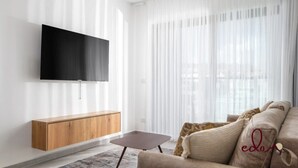 Un soggiorno moderno con una televisione a schermo piatto fissata al muro, un tavolino consolle in legno, un piccolo tavolino da caffè e un divano beige con una coperta decorata.