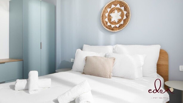 Un letto rifatto con lenzuola bianche e un cuscino color beige, un armadio blu e un arazzo rotondo fatto a mano.