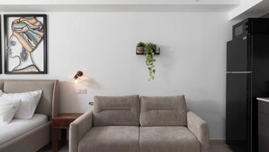 Een moderne woonkamer met een bank, een bijzettafeltje, een wandplant, een ingelijst kunstwerk en een zwarte koelkast.