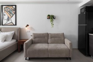 Een moderne woonkamer met een bank, een bijzettafeltje, een wandplant, een ingelijst kunstwerk en een zwarte koelkast.
