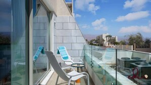 A balcony with glass railings, two lounge chairs, and a small table.