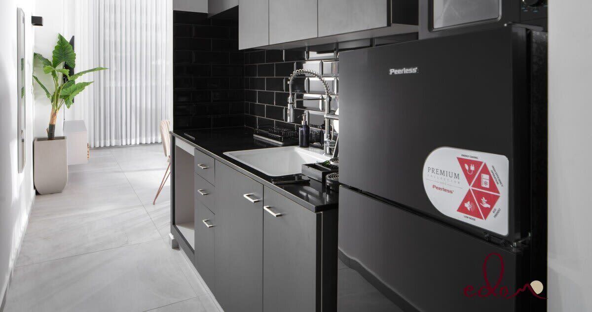 Una cuina moderna amb un refrigerador negre, electrodomèstics d'acer inoxidable i una rebentament de rajoles negres.