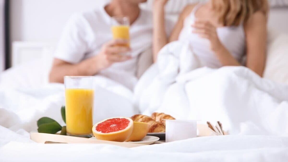Uma mesa de café da manhã com um copo de suco de laranja, meia toranja, um croissant e uma xícara branca em um suporte.