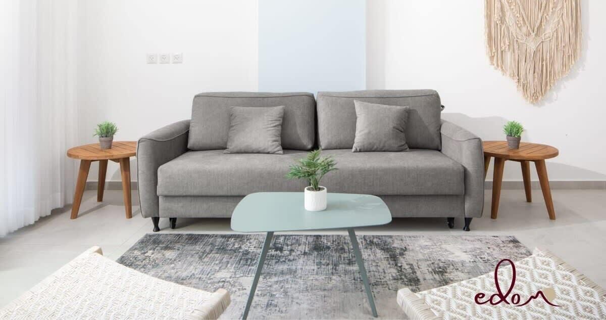 Ett modernt vardagsrum med en grå soffa, två träbord, ett soffbord i glas och en mönstrad matta.