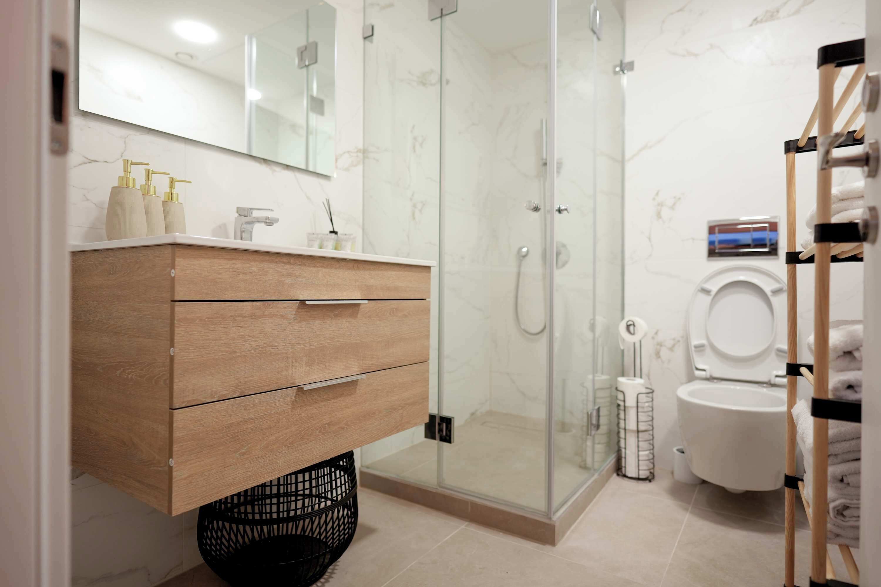 A modern bathroom with a wooden vanity, a glass shower enclosure, and a toilet with a towel rack.