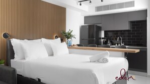 Een moderne slaapkamer met een bed, nachtkastje en uitzicht op een keuken.