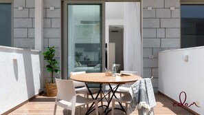 A balcony with a round wooden table, white chairs, a potted plant, and a woven basket. - דירת גן קלאסית בסי סייד 50 מטר מהים - By Edom (Eilat)