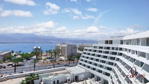 Um hotel moderno com fachada curva, vista para o mar e área de estacionamento com palmeiras.