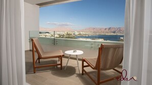 A balcony with two wicker chairs and a small table, overlooking a cityscape and mountains. - דירת 2 חדרי שינה עם נוף מדהים לים - By Edom (Eilat)