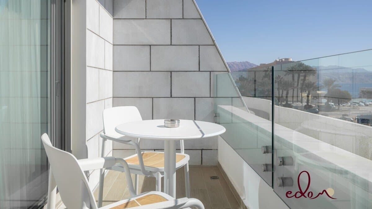 Un balcon doté d’une balustrade en verre, d’une table blanche et de deux chaises blanches.