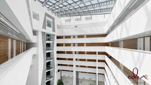A multi-level atrium with a modern design, featuring a central open space with a glass ceiling and wooden panel accents on the walls. - View דירה משפחתית במיקום הטוב באילת (Eilat)