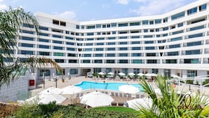 A modern hotel with multiple floors, a central swimming pool, and outdoor seating areas. - View דירה משפחתית במיקום הטוב באילת (Eilat)