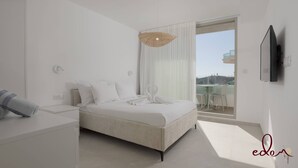 Una camera da letto moderna con un letto grande, un comodino, una televisione a schermo piatto e un balcone con tavolo e sedie.