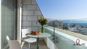 Un balcone con un tavolo in vetro, due sedie bianche, un vaso con fiori e croissant.