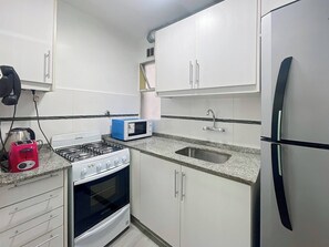A compact kitchen with white cabinets, a gas stove, a microwave, a sink, and a refrigerator. - Charming Apartment in Recoleta 4 pax (Buenos Aires)