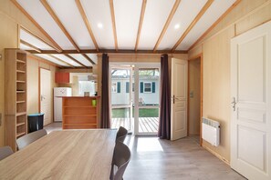 A room with a wooden ceiling, a dining table, chairs, a white radiator, and a sliding glass door leading to an outdoor area. - Chalet “Le Convivial Cottage” with Shared Pool, Wi-Fi, and Air Conditioning (Saint-Martial-de-Nabirat)