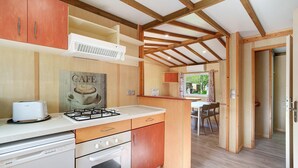 A kitchen with wooden beams, a toaster, a gas stove, and a dining area with chairs. - Chalet “Le Convivial Cottage” with Shared Pool, Wi-Fi, and Air Conditioning (Saint-Martial-de-Nabirat)