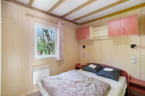 Une chambre à coucher avec un lit, une fenêtre avec des rideaux, un radiateur et des armoires en bois.