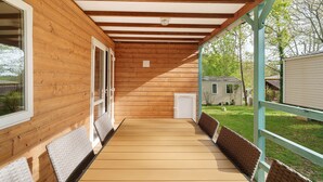 A wooden deck with a covered area, wicker furniture, and a view of a house in the background. - Chalet “Le Convivial Cottage” with Shared Pool, Wi-Fi, and Air Conditioning (Saint-Martial-de-Nabirat)