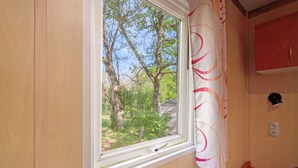 A window with a view of trees and a house, a wooden wall, and a red cabinet. - Chalet “Le Convivial Cottage” with Shared Pool, Wi-Fi, and Air Conditioning (Saint-Martial-de-Nabirat)