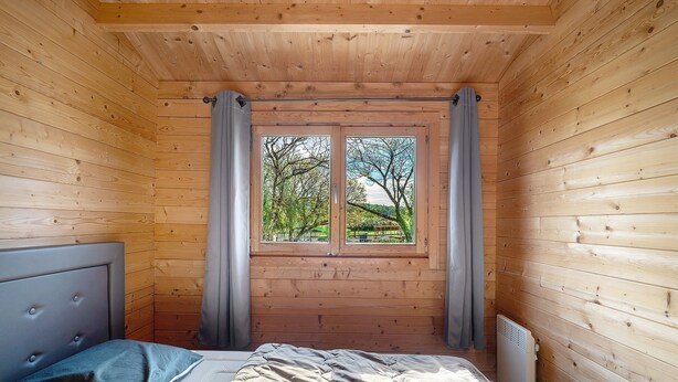 Une pièce de cabane en bois comprenant un lit, des rideaux et une fenêtre donnant sur la forêt.