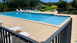 Une piscine avec un toboggan, des chaises longues et une zone délimitée par une clôture.