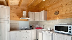 Une cuisine avec des murs en bois, des placards blancs, une cuisinière à gaz, une machine à café et un four à micro-ondes.