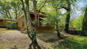 Eine Holzhütte mit einer Holzterrasse, umgeben von Bäumen und einer Wiese.