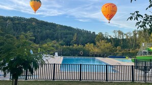 Ein Swimmingpool mit umgebendem Zaun, Bäumen und Heißluftballons im Hintergrund.