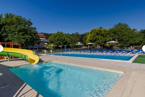 A swimming pool with a slide, lounge chairs, and a fenced area.