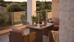 Ein Balkon mit Korbmöbeln, einem Tisch gedeckt mit einem Weinglas und Blick auf Grünflächen.
