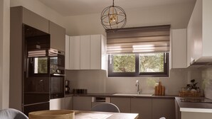 Eine moderne Küche mit Essbereich, ausgestattet mit Backofen, großem Fenster mit Jalousien und einer Pendelleuchte.
