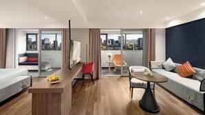 Ein modernes Hotelzimmer mit Blick auf die Stadt, einem Essbereich, einer Couch und einem kleinen Tisch.
