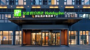 Der Eingang eines Holiday Inn Express Hotels mit modernem Design, inklusive Glasfassade und einem auffälligen, grünen Logo.