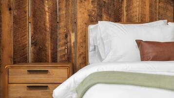 Uma mesa de cabeceira de madeira com gavetas, uma cama com roupa de cama branca e um cobertor verde, e uma parede de madeira.
