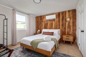 Ein Schlafzimmer mit Holzpaneelen, einem Bett mit weißer Bettwäsche, einem Nachttisch mit Lampe und einem Fenster mit Vorhängen.