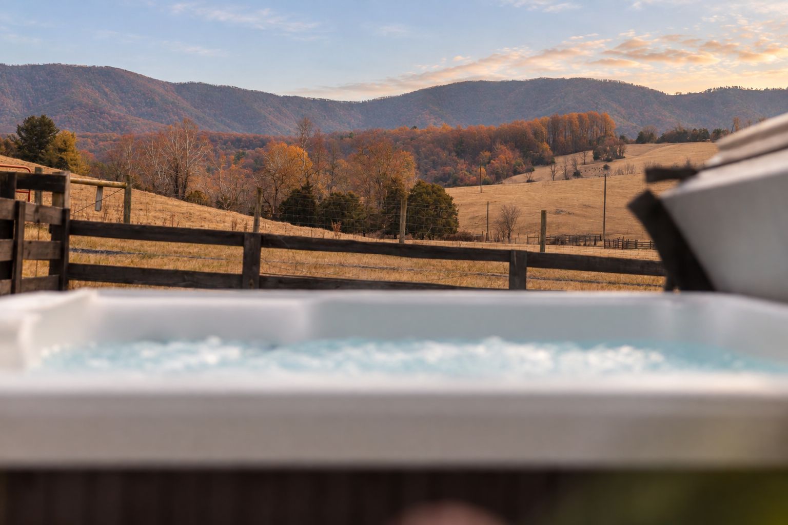 A hot tub with a view of a hilly landscape and a wooden fence.