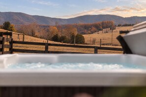 A hot tub with a view of a hilly landscape and a wooden fence.