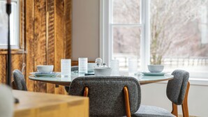 A dining table with chairs, a window with a view of trees, and a wooden wall. - The Writer's Cottage - 13m to Shenandoah NP, Hot Tub, Mountain Views, EV (Luray)