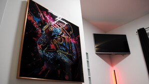 A framed artwork of a lion's face on a wall, a flat-screen TV mounted above it, and a red light fixture. - QT suite & luxury (Rome)