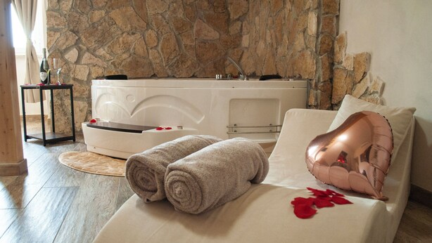 A bedroom with a stone wall, a bathtub, and a bed with towels and rose petals. - QT suite & luxury (Rome)