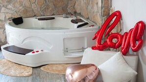 A spa room with a stone wall, a white bathtub, and a white sofa with rose petals and a 'Love' balloon. - QT suite & luxury (Rome)