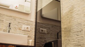 A modern bathroom with a stone backsplash, a wooden cabinet, and a glass shower enclosure. - QT suite & luxury (Rome)