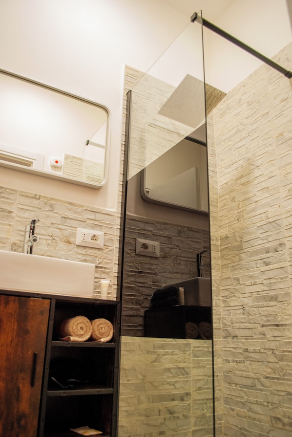 A modern bathroom with a stone backsplash, a wooden cabinet, and a glass shower enclosure. - QT suite & luxury (Rome)