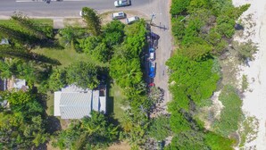 An aerial view of a property with a paved road, parked vehicles, and dense greenery. - By The Sea - by Lifestyle. Brunswick Heads (NEW BRIGHTON)